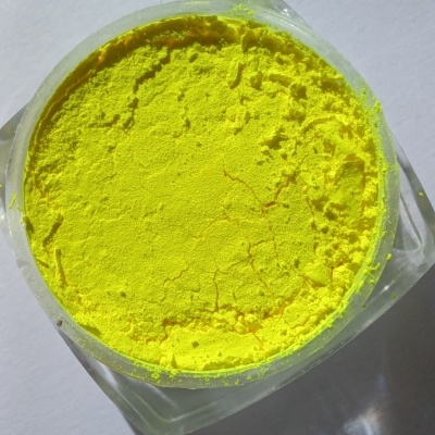 Pó pigmento amarelo dentro de recipiente plástico transparente sobre superfície branca