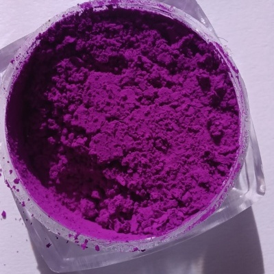 Pó violeta intenso em recipiente transparente sobre superfície branca com sombra.