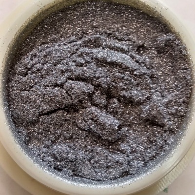 Pote com pó cinza prateado sobre superfície com padrão de folhas verdes