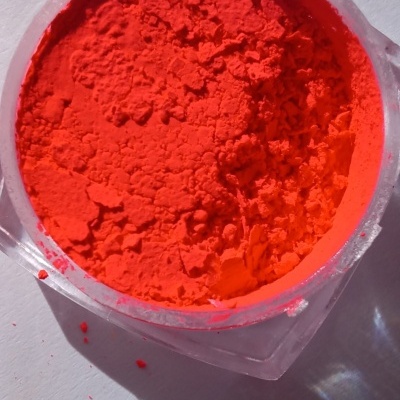 Pó pigmento laranja fluorescente em recipiente transparente sobre superfície branca