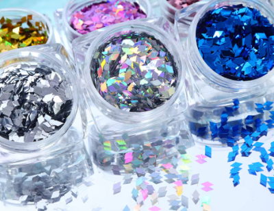 Potes de glitter colorido metálico espalhados numa superfície espelhada