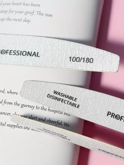 Três lixas de unhas cinza claro com texto escrito preto sobre uma página de livro