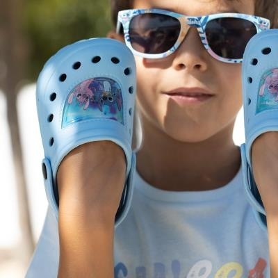 Sapatilhas Crocs azuis para criança com flamingos, usadas por menino com óculos de sol.