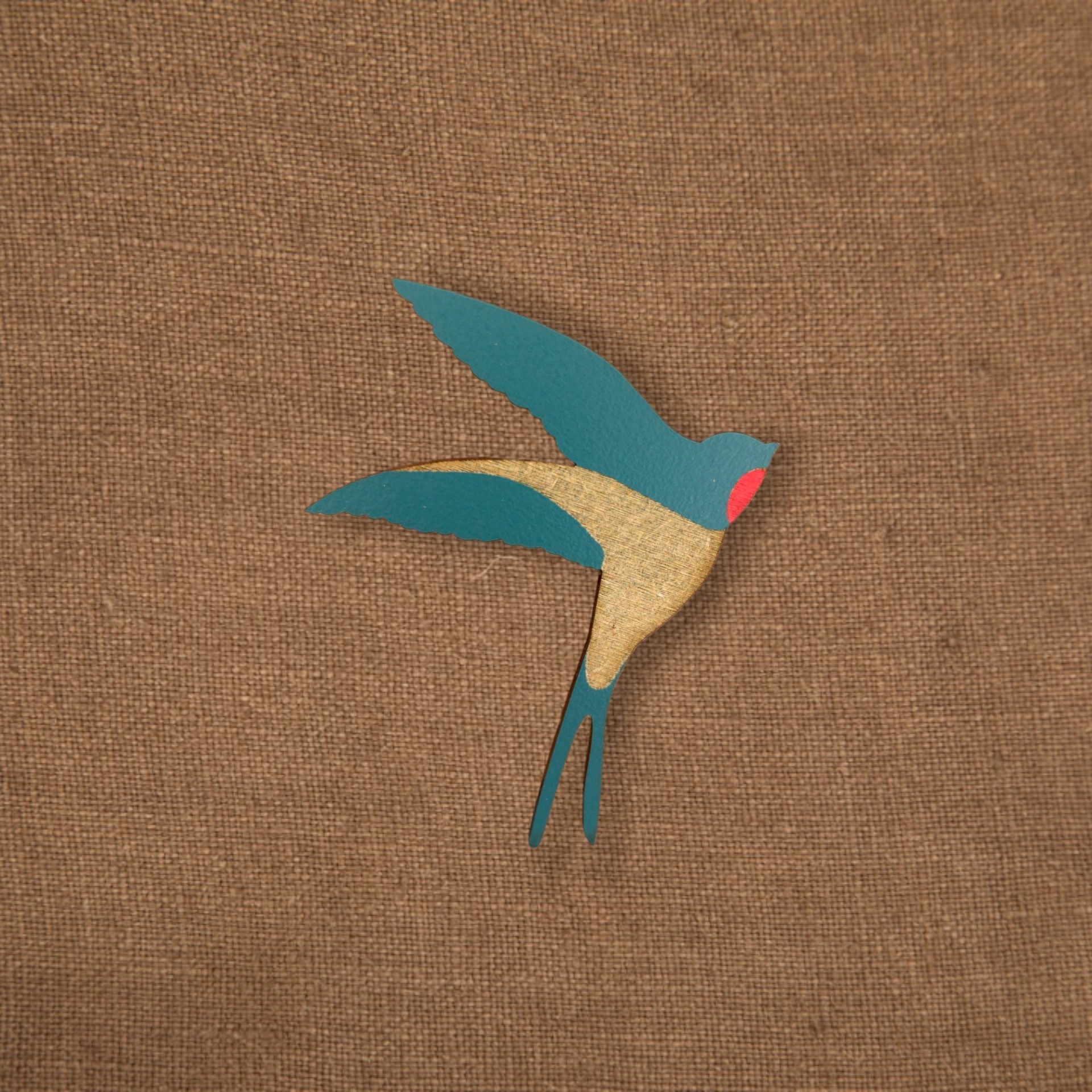 Pregadeira Andorinha Figura decorativa de pássaro pintada em azul, bege e vermelho sobre tecido castanho