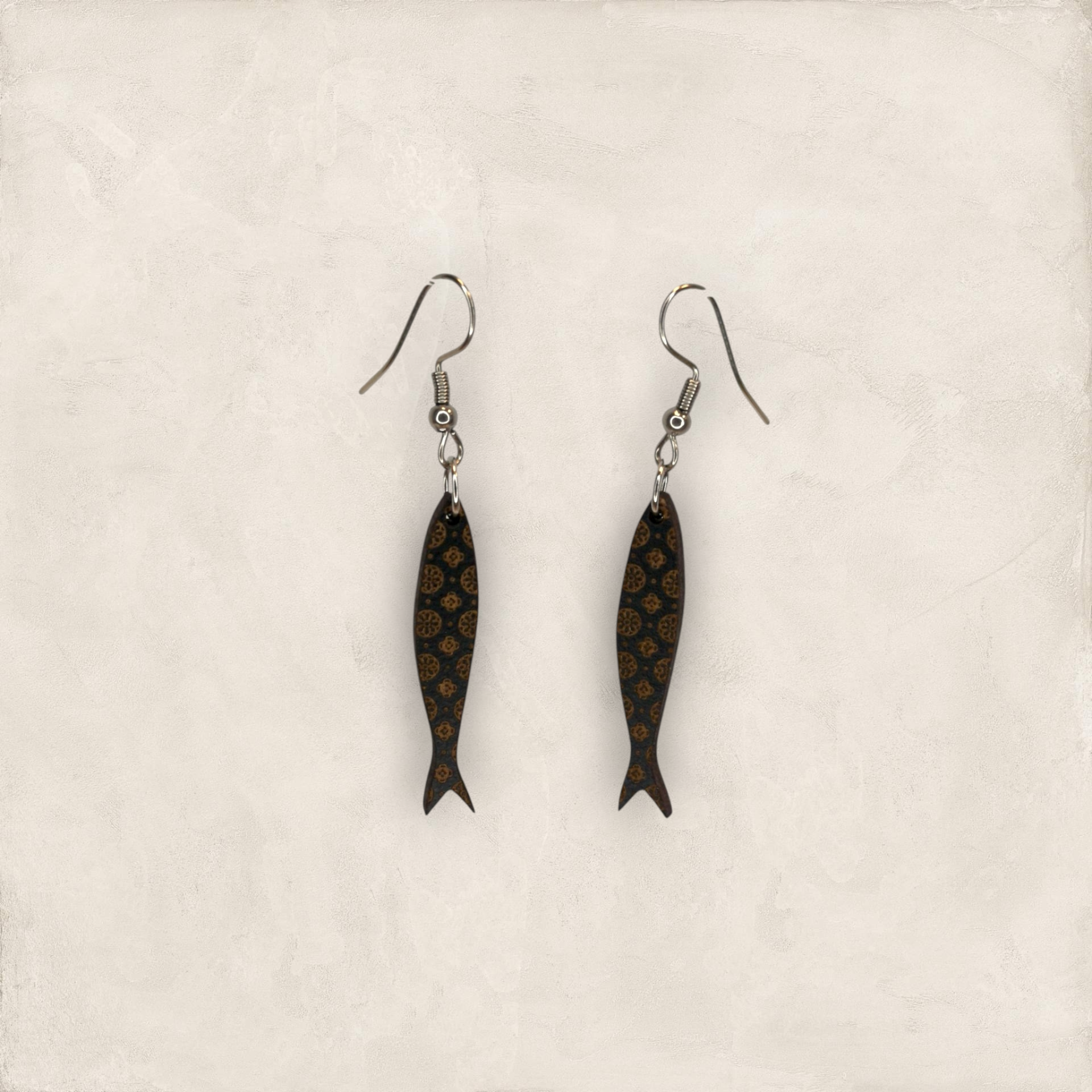 Brincos Sardinha Gravada Brincos em forma de peixe com padrão castanho sobre fundo preto e gancho metálico prateado.