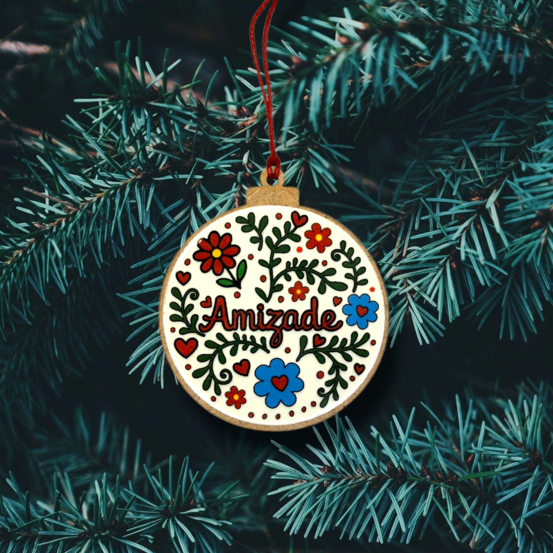 Bola de Natal "Amizade" Ornamento circular em madeira com decoração floral e texto Amizade, pendurado num pinheiro