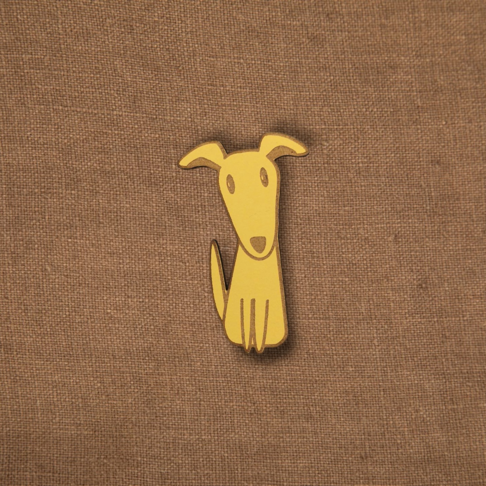 Pregadeira Cão Pino decorativo amarelo em forma de cão num tecido castanho