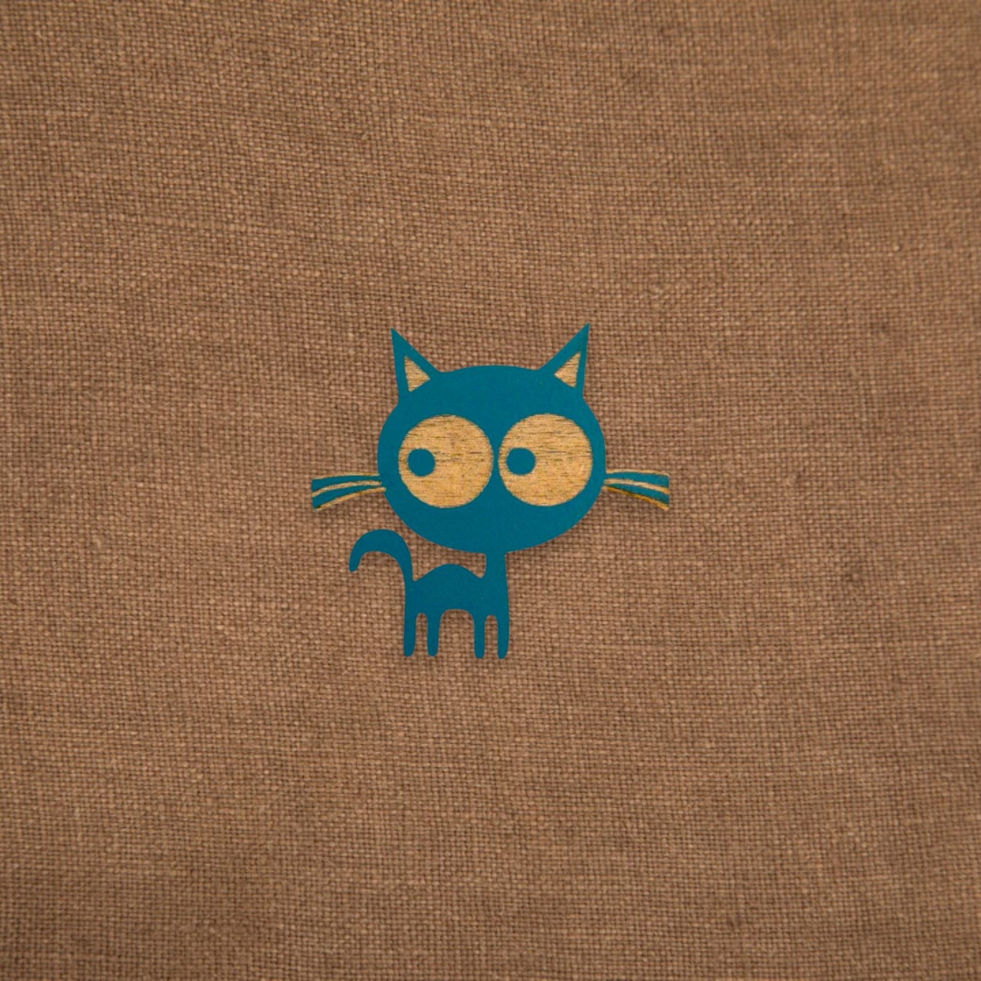 Pregadeira Sr. Gato Desenho de gato azul estilizado com olhos grandes sobre fundo de tecido castanho