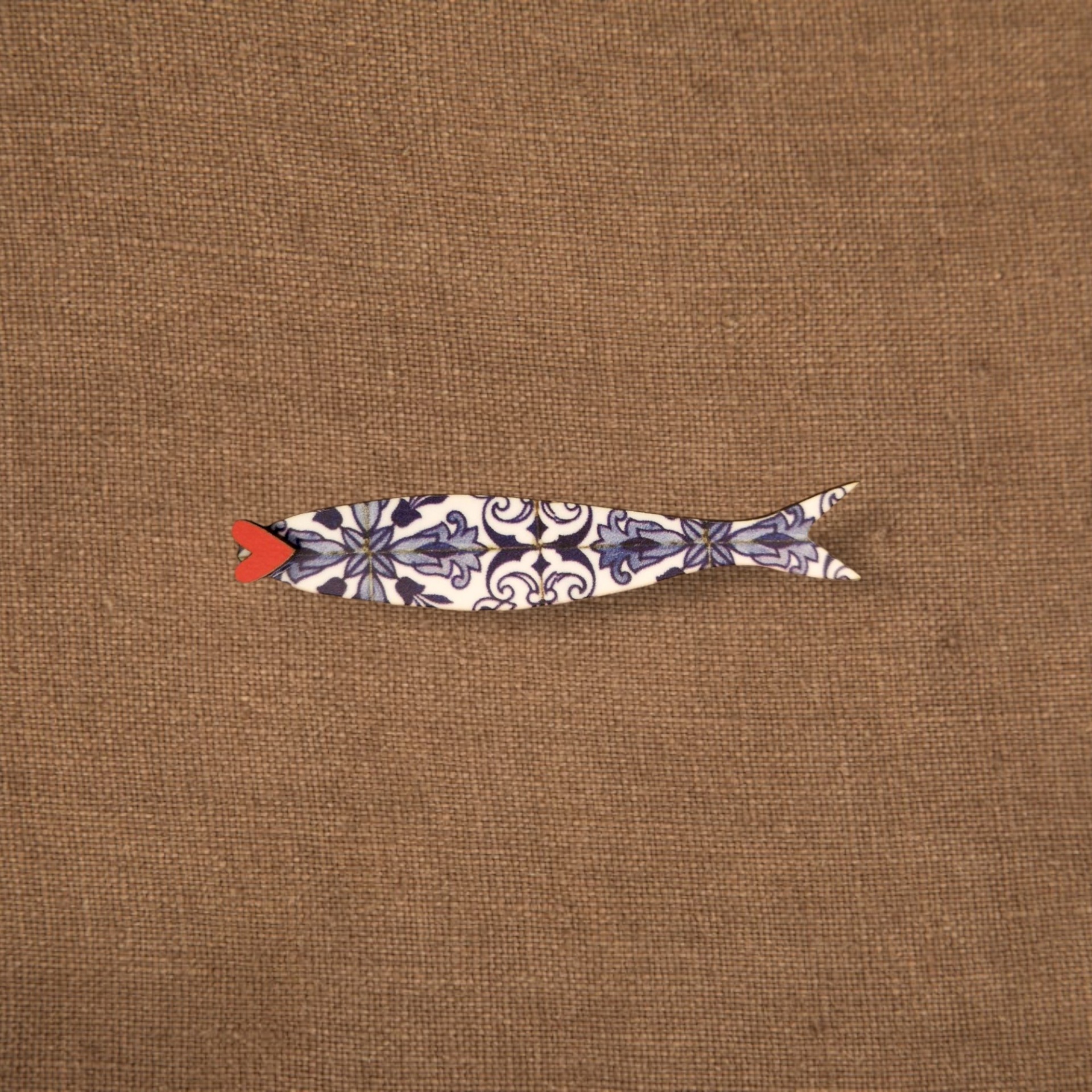Pregadeira Sardinha Azulejo Figura decorativa em forma de peixe com padrão azul e branco sobre tecido castanho