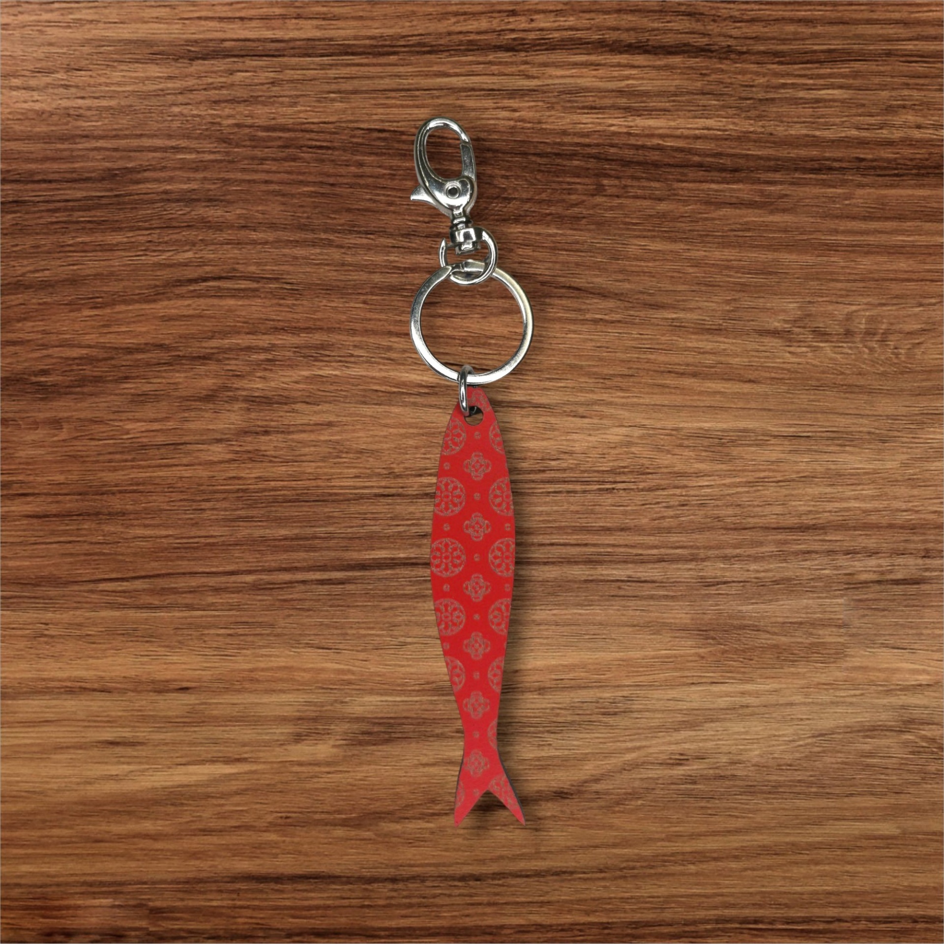 Porta-chaves Sardinha Gravada Porta-chaves em forma de peixe vermelho com padrão dourado sobre fundo de madeira
