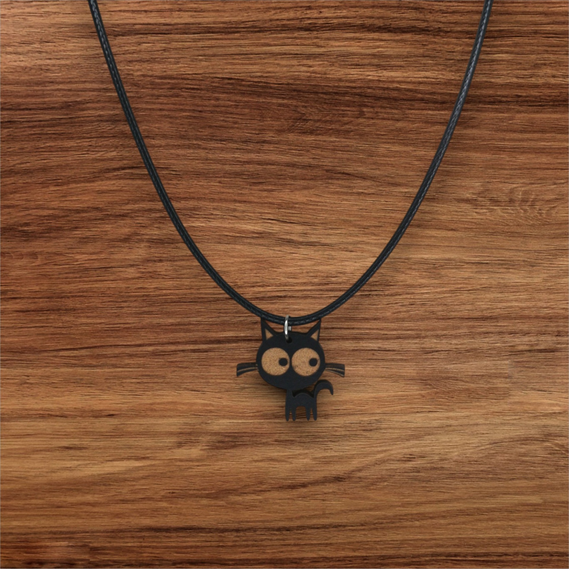 Colar Sr. Gato Colar com pendente de gato preto de olhos grandes sobre superfície de madeira.