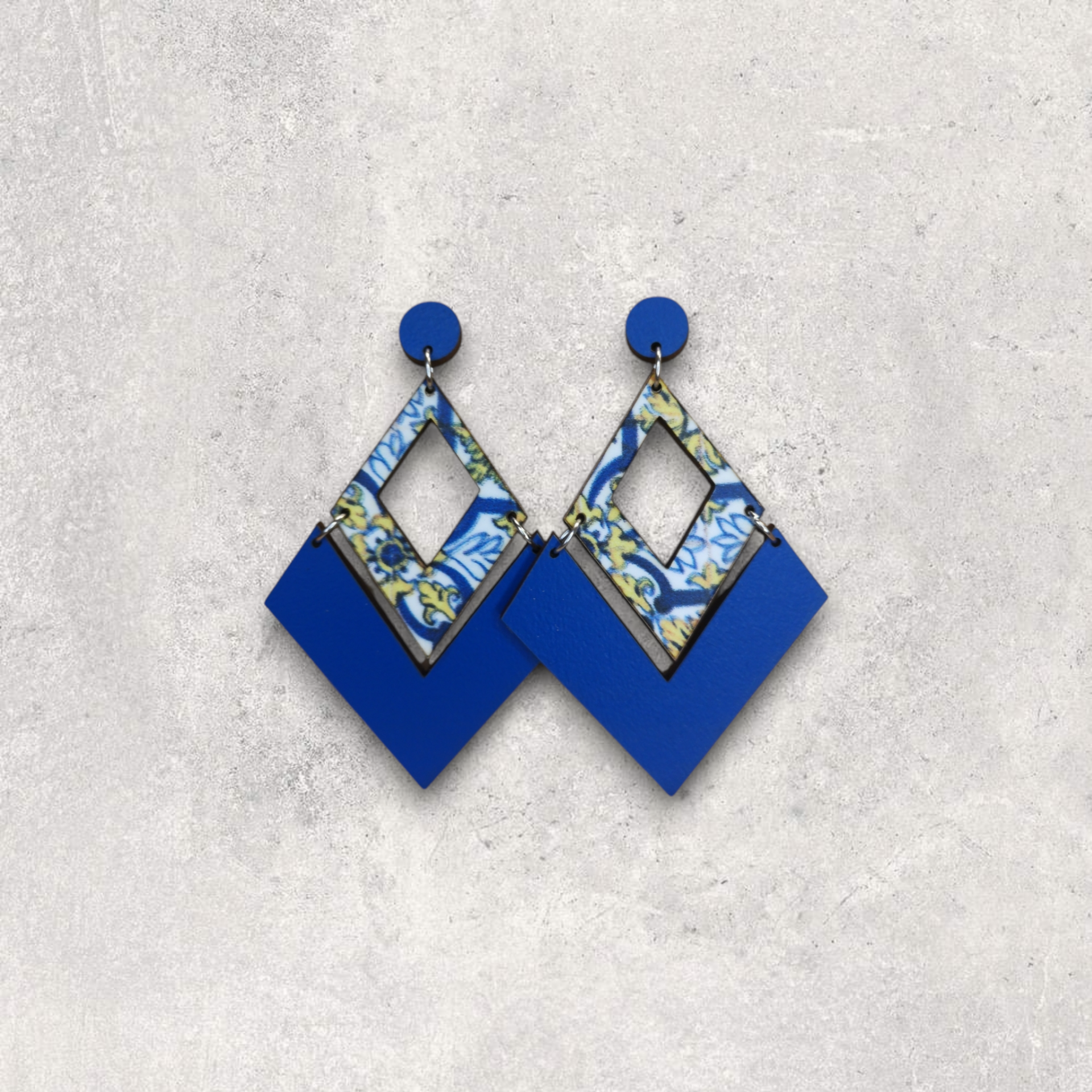 Brincos Caldas da Rainha Brincos pendentes em azul e padrão floral sobre fundo cinzento.