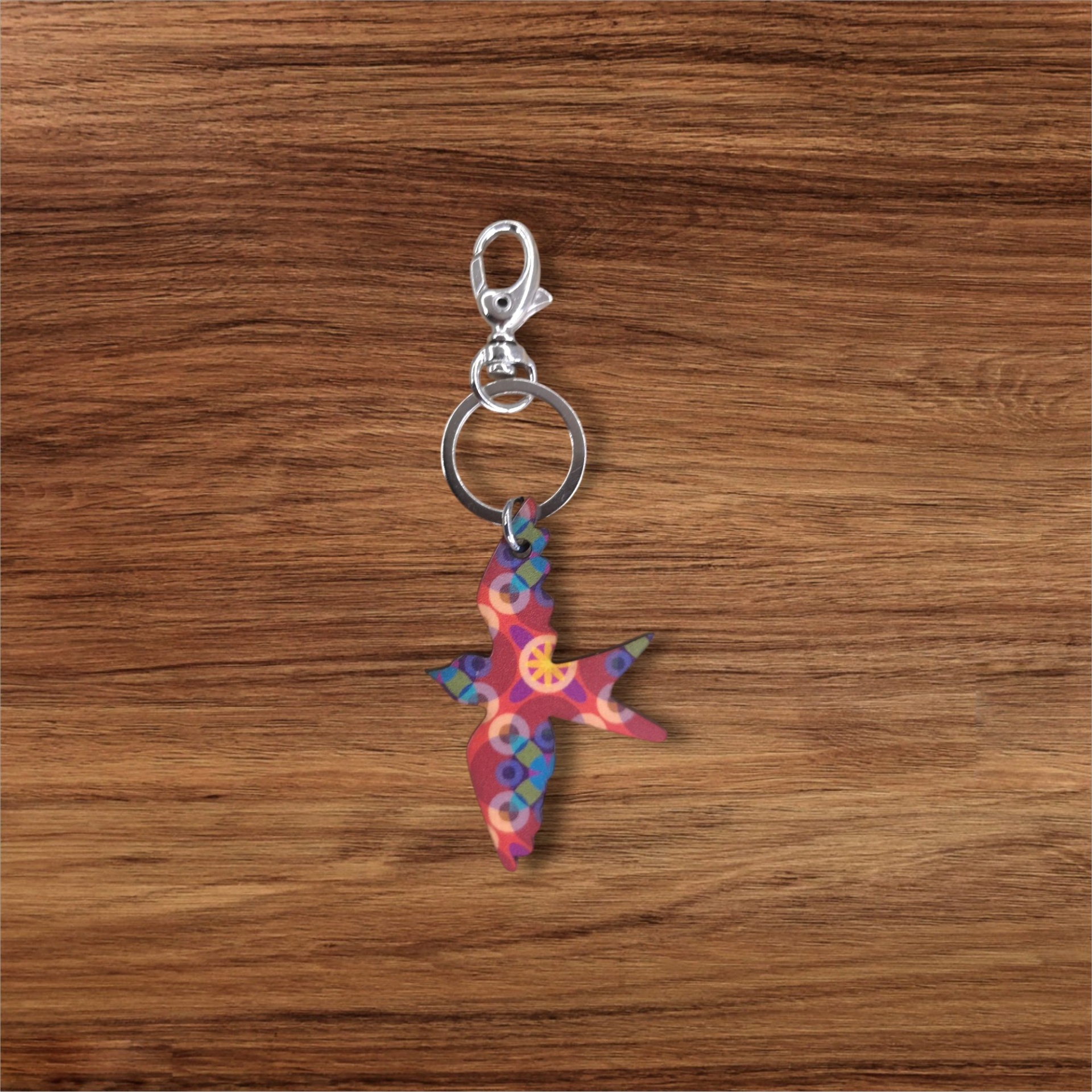 Porta-chaves Andorinha Chaveiro metálico com pendente colorido em forma de pássaro numa superfície de madeira