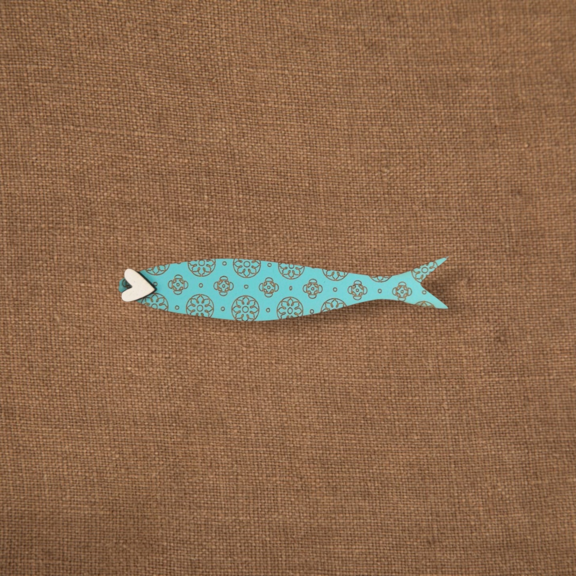 Pregadeira Sardinha Figura decorativa de peixe azul com padrões sobre tecido castanho.