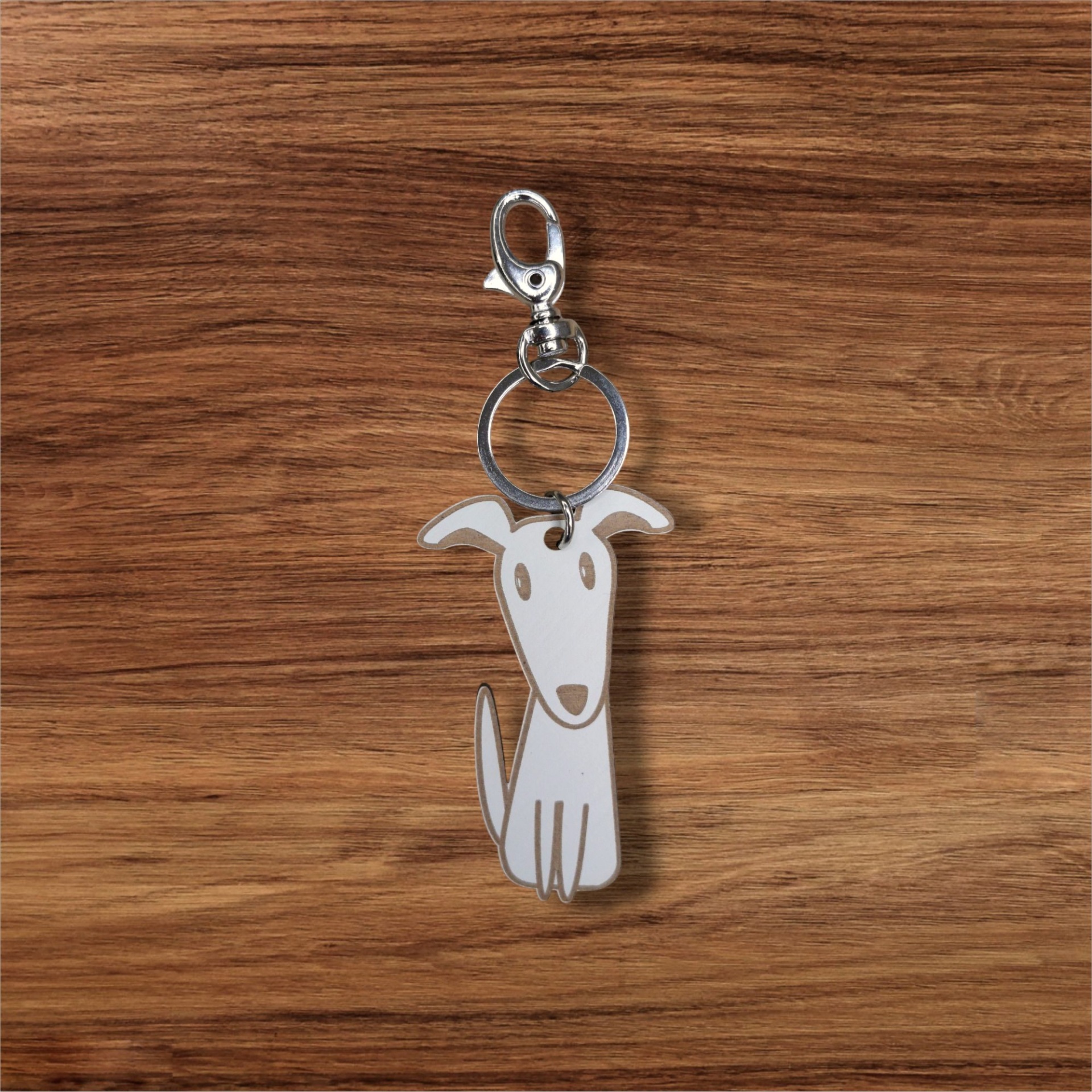 Porta-chaves Cão Porta-chaves com pendente em forma de cão branco com olhos e contornos cinzentos sobre madeira clara