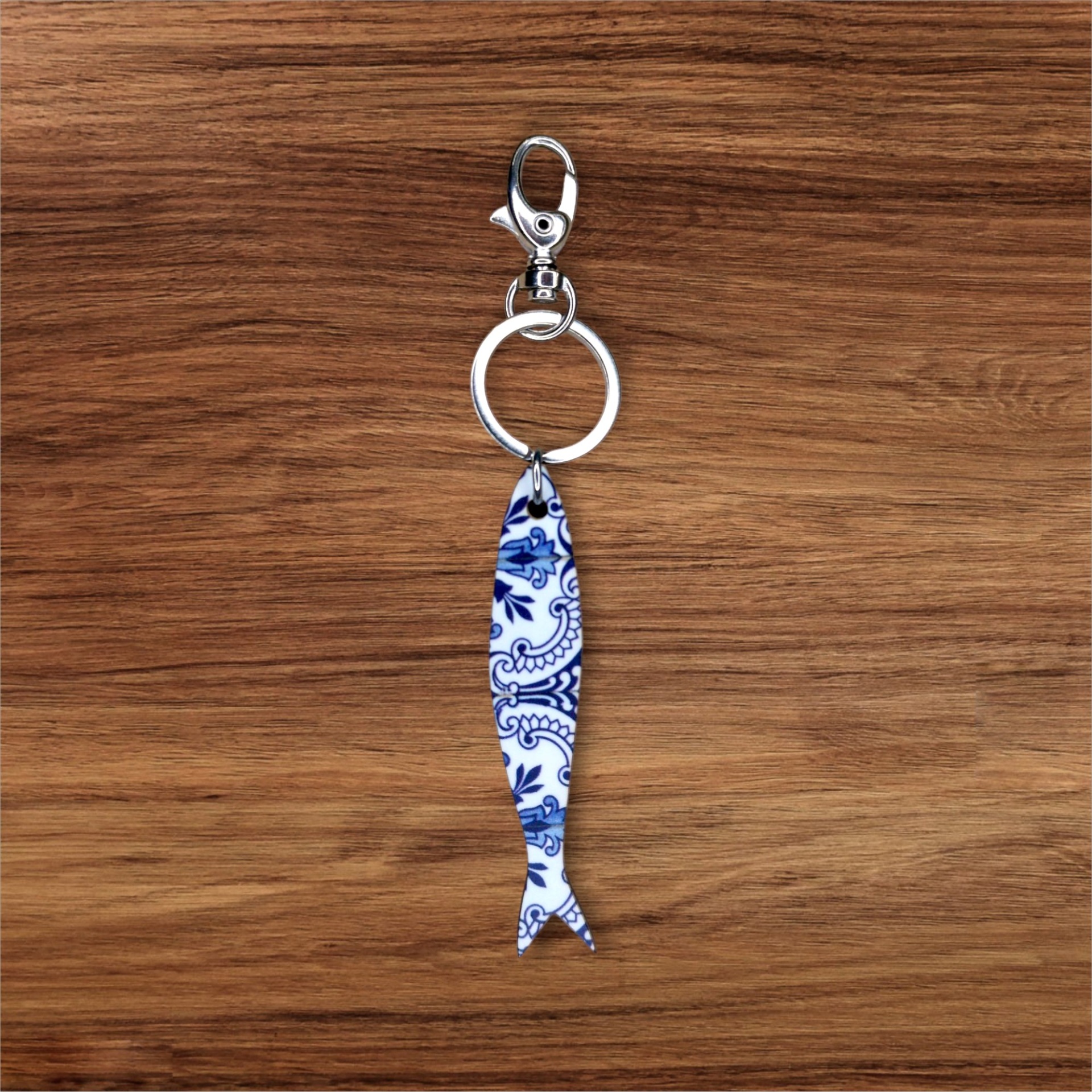 Porta-chaves Sardinha Azulejo Porta-chaves com pendente de peixe em cerâmica com padrão azul e branco sobre madeira.