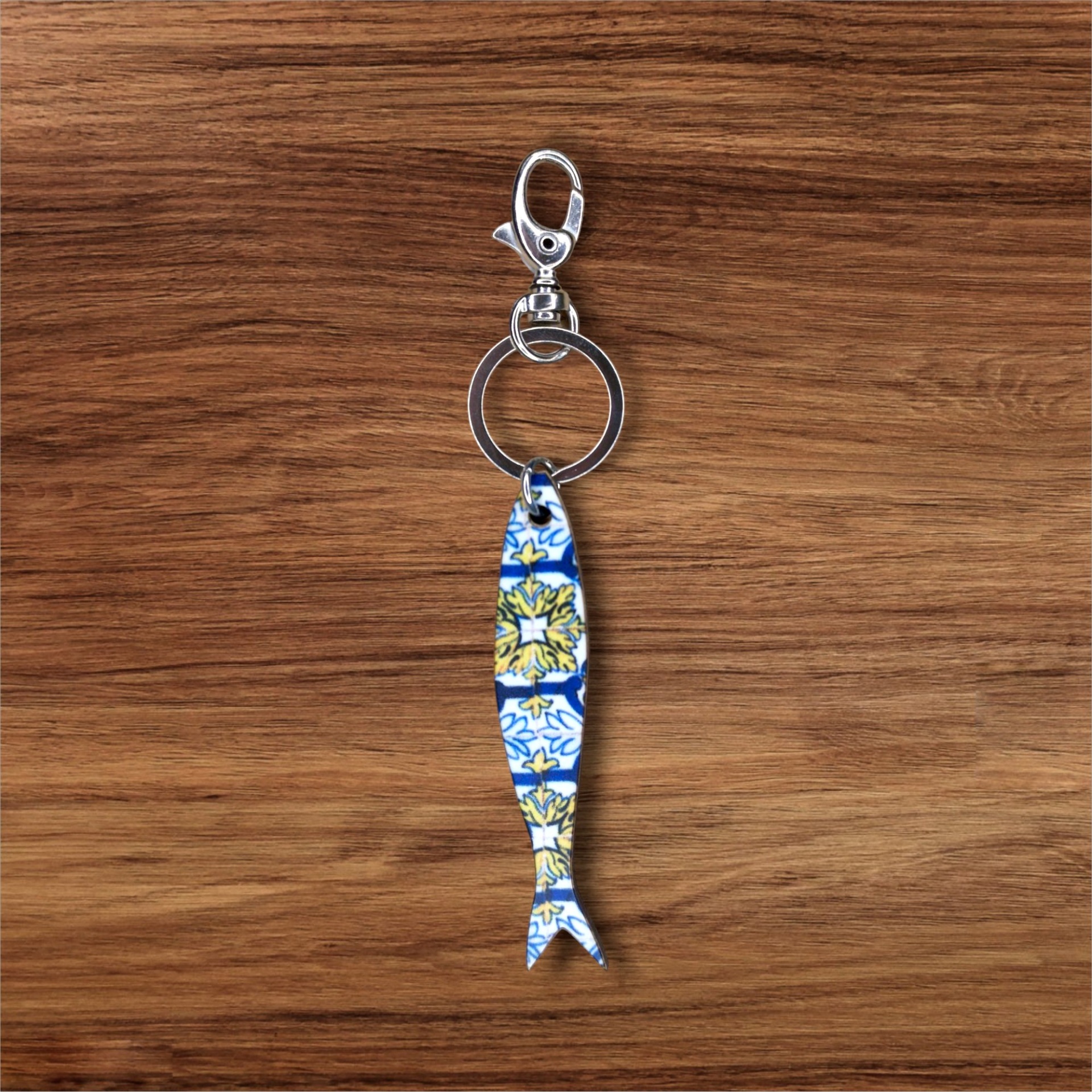 Porta-chaves Sardinha Azulejo Porta-chaves com pendente em forma de peixe com padrão azul, branco e amarelo sobre madeira