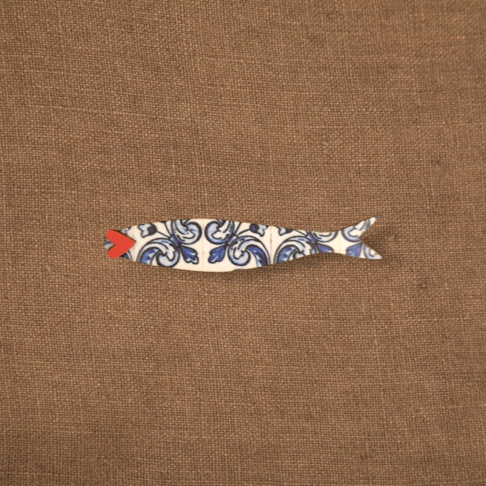 Pregadeira Sardinha Azulejo Figura decorativa em forma de peixe com padrão azul e branco num tecido castanho