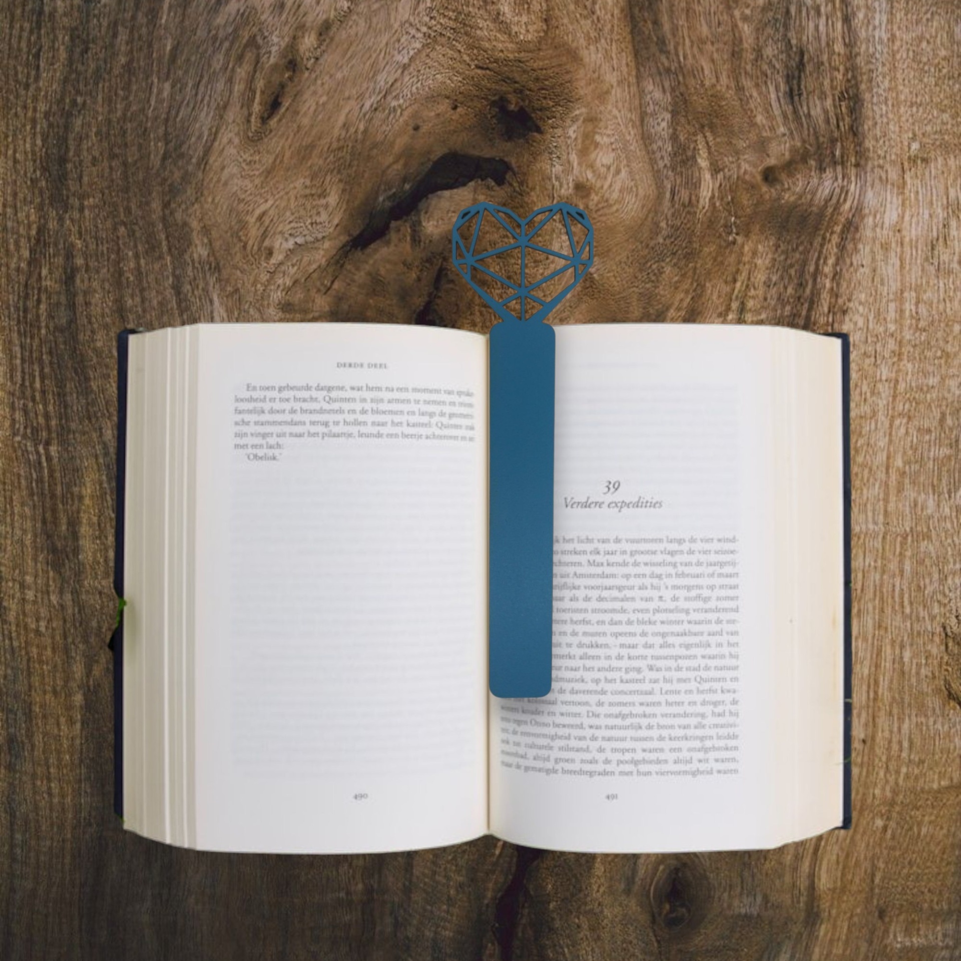Marcador Coração Origami Marcador de livros azul em forma de coração geométrico num livro aberto sobre mesa de madeira