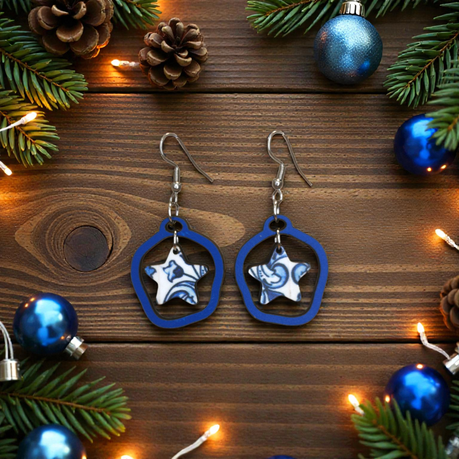 Brincos Estrela Brincos de estrela azul e branca com estrutura azul em fundo de madeira, decorados com elementos natalícios