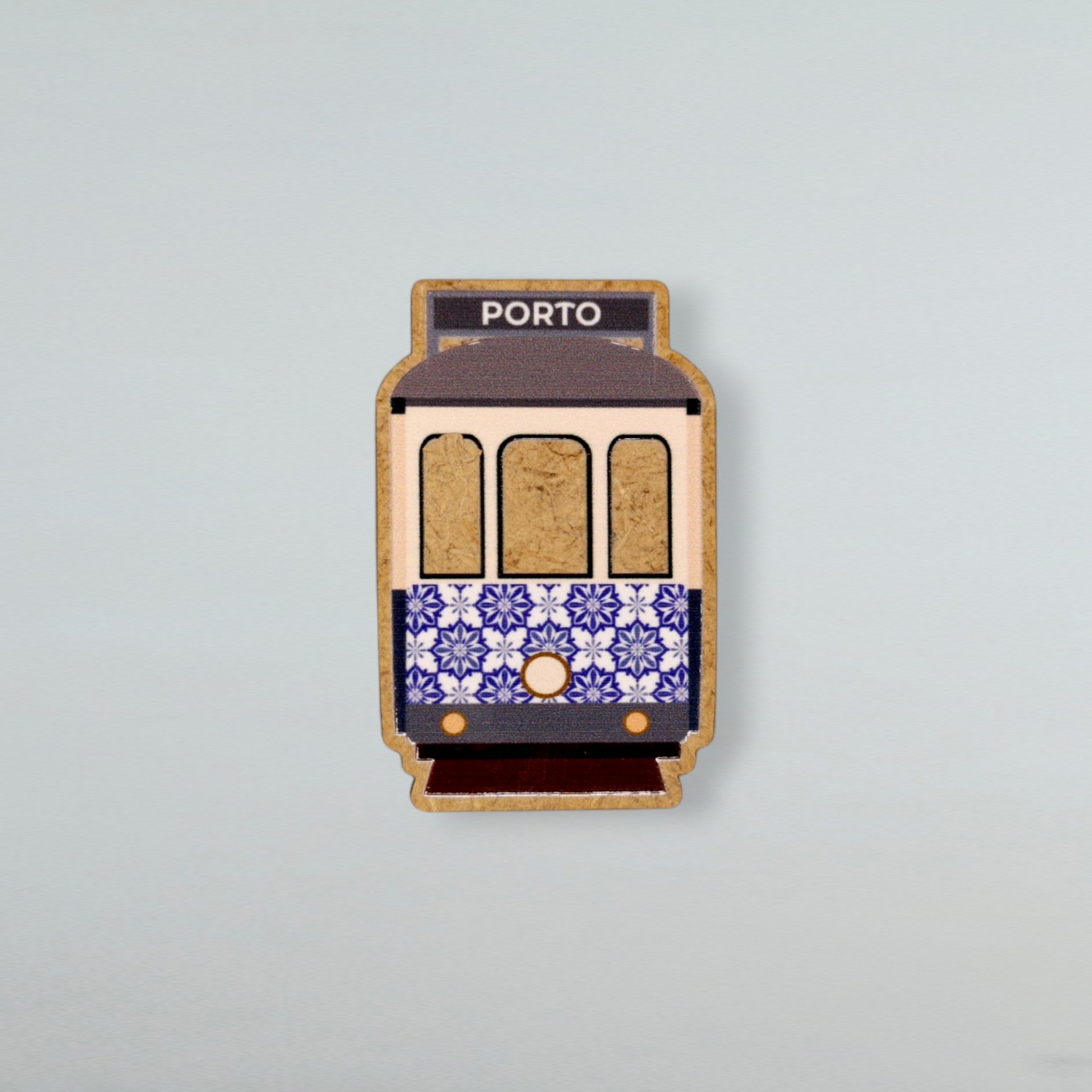 Magnético Elétrico com Azulejo Produto em cortiça com forma de elétrico decorado com padrão azulejar azul e branco e texto 'PORTO' topo.