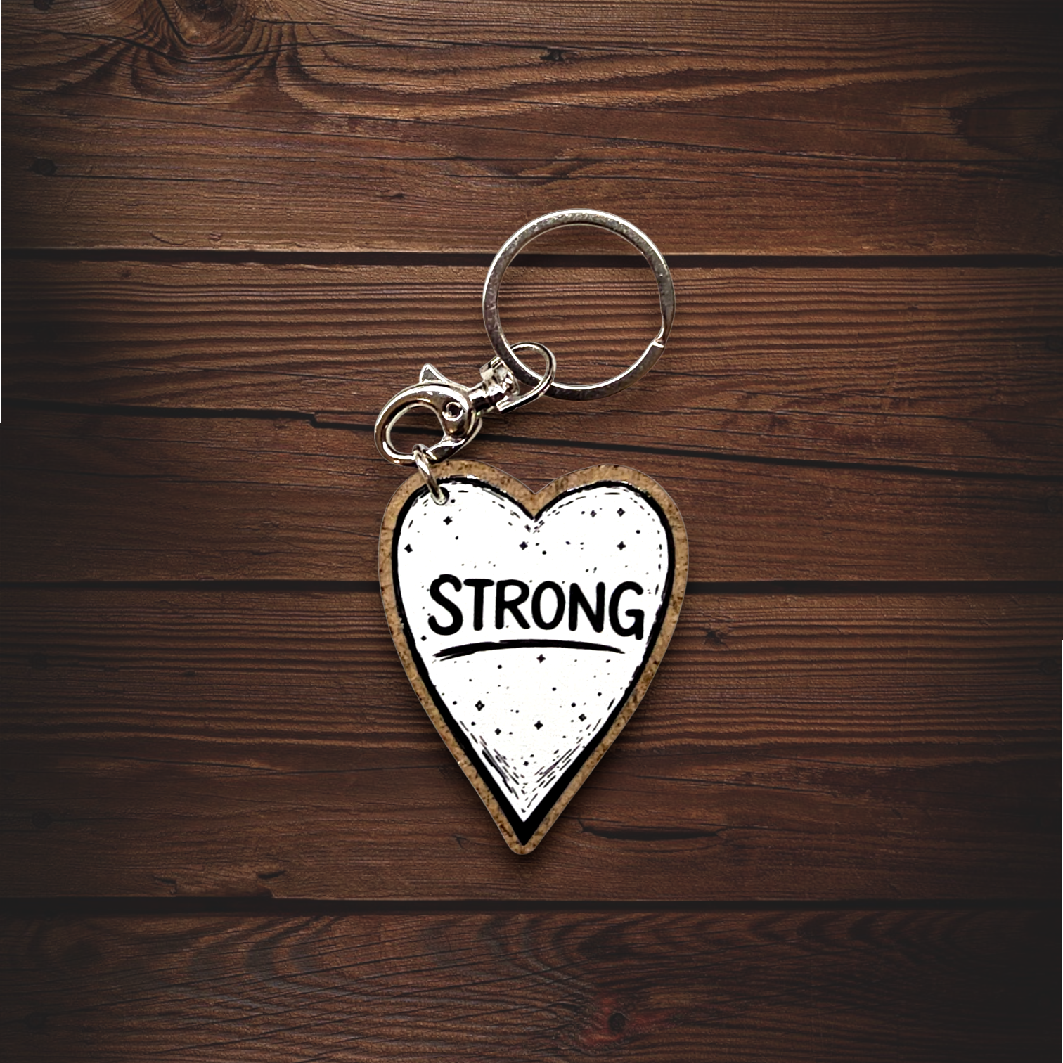 Porta-chaves Coração Mulher "Strong" Porta-chaves metálico com pendente em forma de coração branco com texto STRONG sobre madeira castanha