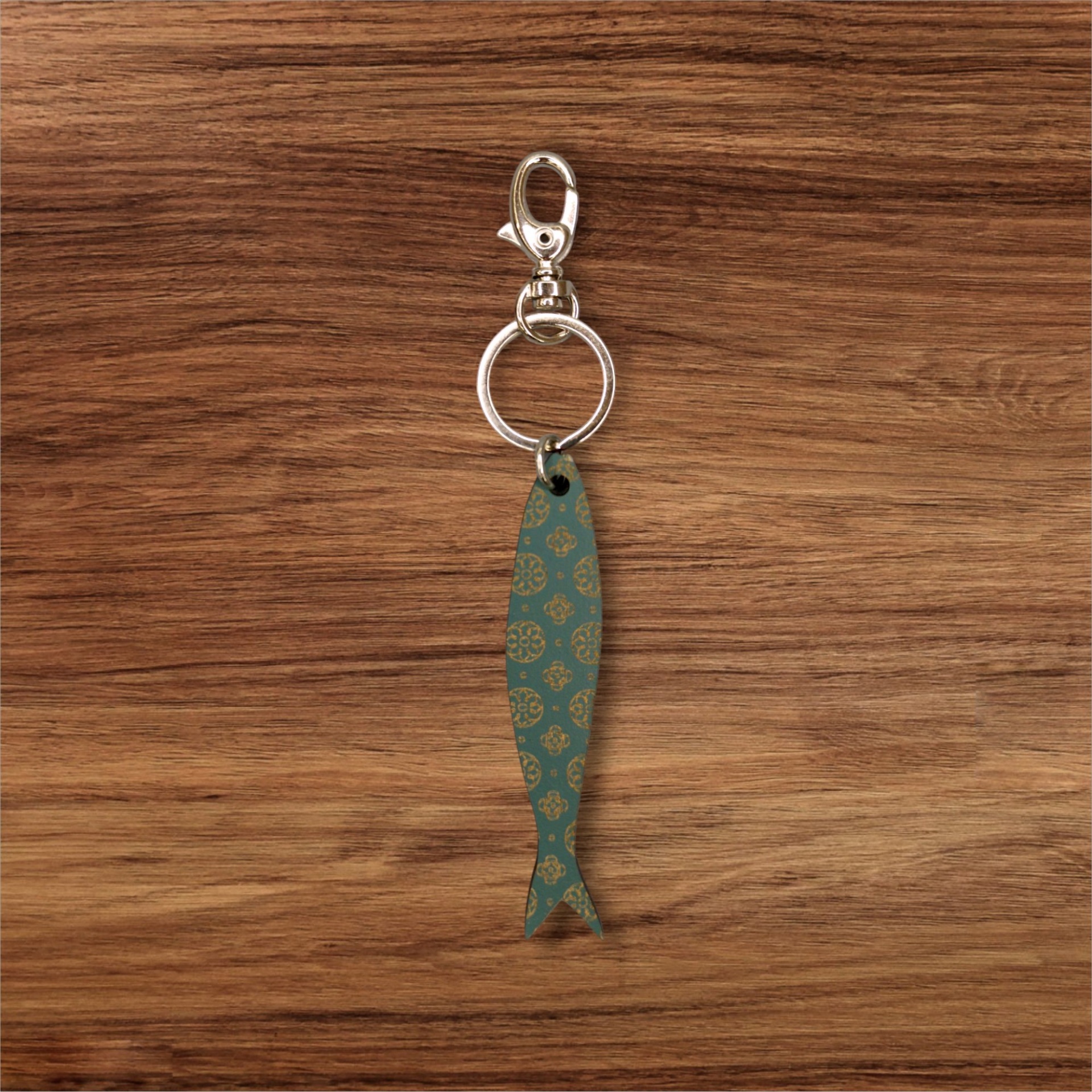 Porta-chaves Sardinha Gravada Chaveiro com pingente de peixe azul com padrão dourado sobre fundo de madeira