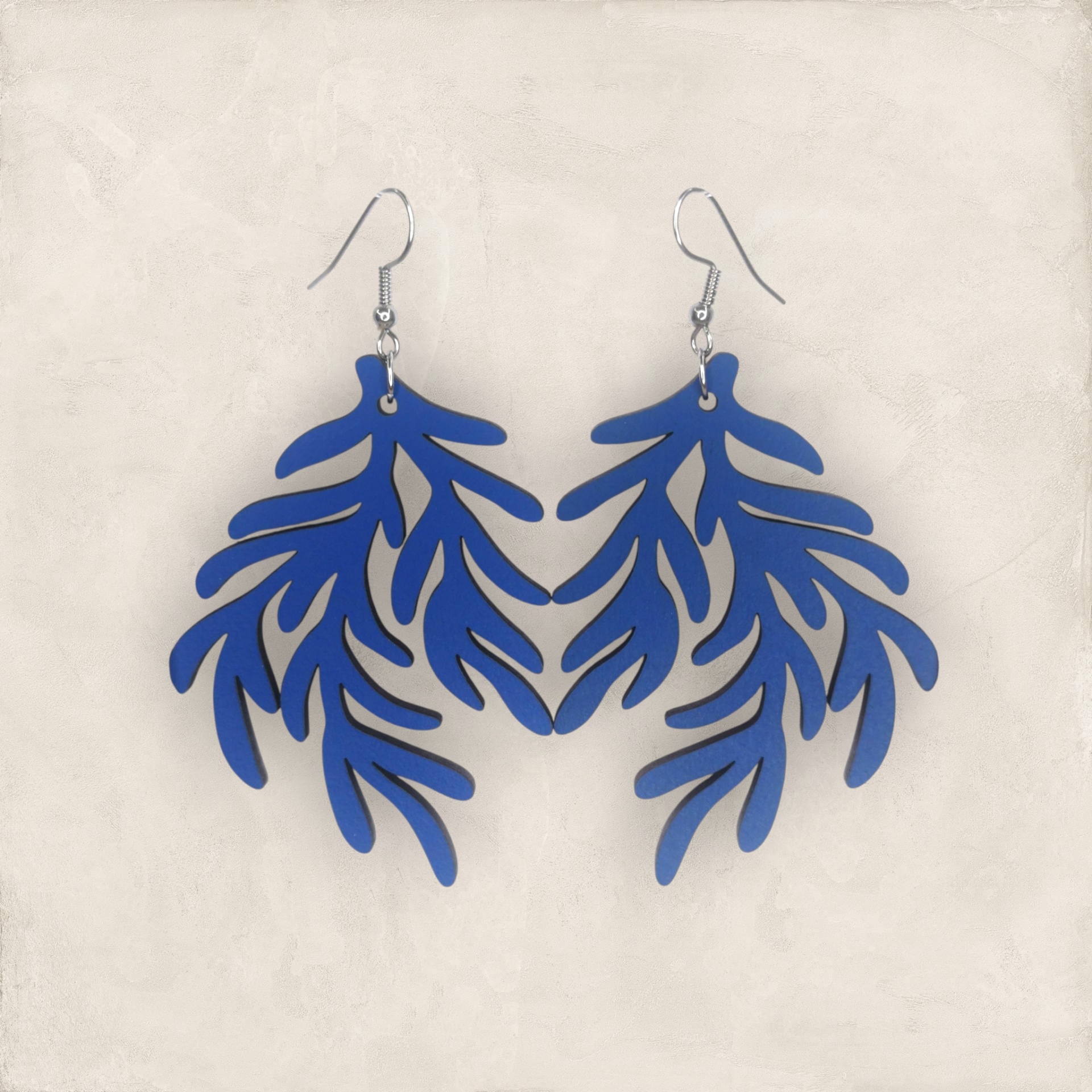Brincos Rama Brincos pendentes azuis com formato de folhas em fundo bege
