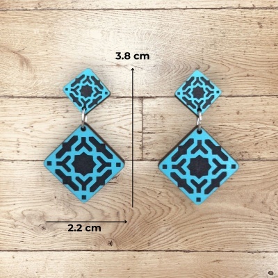 Brincos pendentes azul e preto geométricos sobre madeira clara