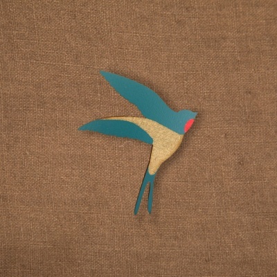 Figura decorativa de pássaro pintada em azul, bege e vermelho sobre tecido castanho