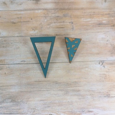 Dois brincos triangulares em madeira azul com recortes geométricos sobre superfície de madeira clara