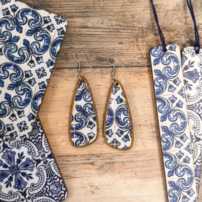 Brincos com padrão azul e branco inspirado em azulejos portugueses e outros objetos com padrão similar em fundo de madeira.