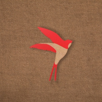 Adorno de pássaro de madeira vermelho e natural sobre tecido castanho texturizado