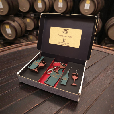 Conjunto de acessórios de cortiça com tema de vinho do Porto numa caixa aberta sobre um barril de madeira