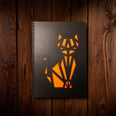 Caderno preto com desenho de gato geométrico em laranja sobre madeira.
