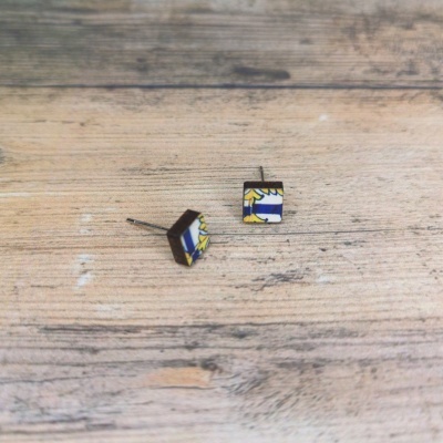 Brincos quadrados com padrão azul, amarelo e branco sobre madeira