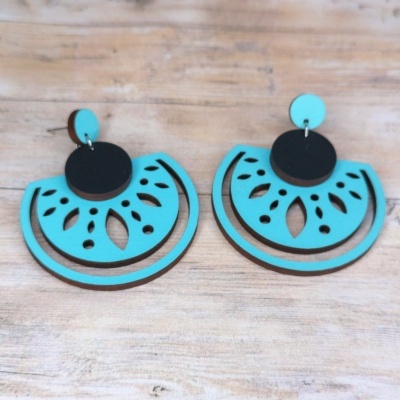 Brincos de madeira turquesa e preta com recortes orgânicos sobre mesa de madeira.