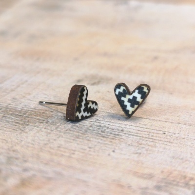 Brincos em forma de coração com padrão preto e branco em zigzag e cruz sobre superfície de madeira.