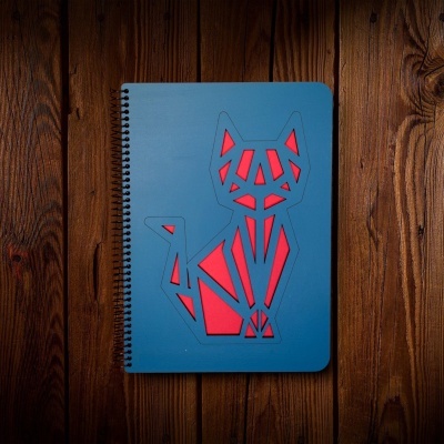 Caderno azul com recortes de gato e fundo vermelho sobre madeira marrom