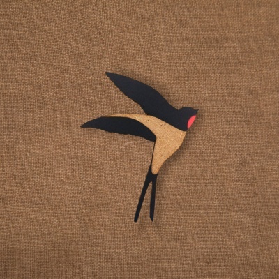 Broche de andorinha em cortiça e preto com detalhe vermelho, sobre tecido castanho
