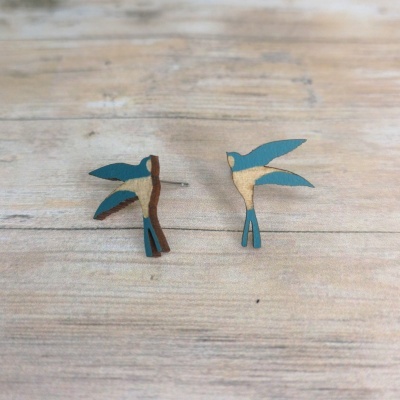 Brincos em forma de pássaros azul e bege sobre madeira clara