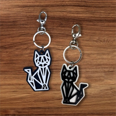 Dois porta-chaves de madeira com design geométrico de gato preto e branco sobre fundo de madeira.