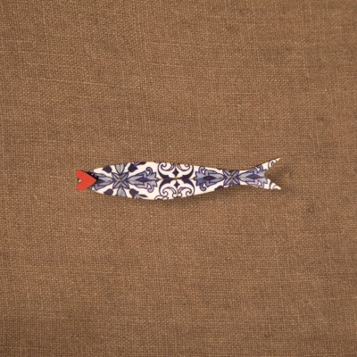 Figura decorativa em forma de peixe com padrão azul e branco sobre tecido castanho