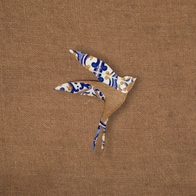 Pássaro de madeira com padrão azulejo português sobre tecido de juta castanho