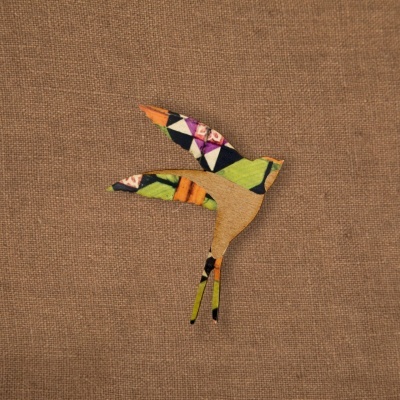 Pássaro decorativo em madeira com asas de tecido colorido em fundo castanho