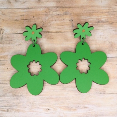 Brincos verdes em forma de flor com recorte ao centro sobre madeira clara.