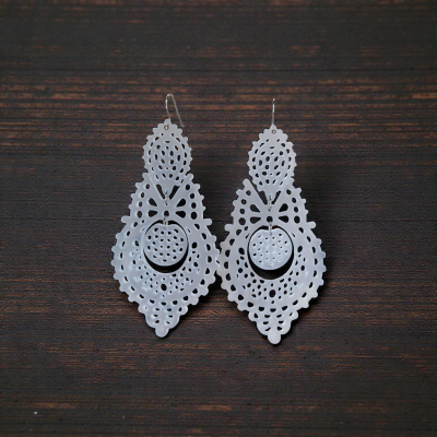 Brincos pendentes brancos com padrão recortado e furos, sobre fundo de madeira escura