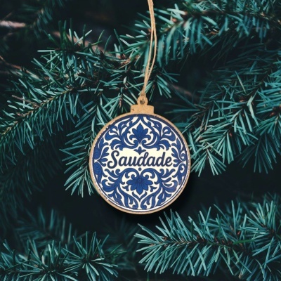 Ornamento redondo azul e branco com palavra Saudade pendurado numa árvore de Natal