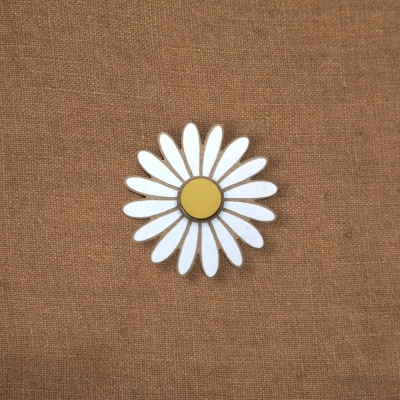 Broche em forma de flor margarida branca com centro amarelo sobre fundo castanho