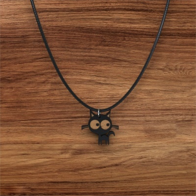 Colar com pendente de gato preto de olhos grandes sobre superfície de madeira.